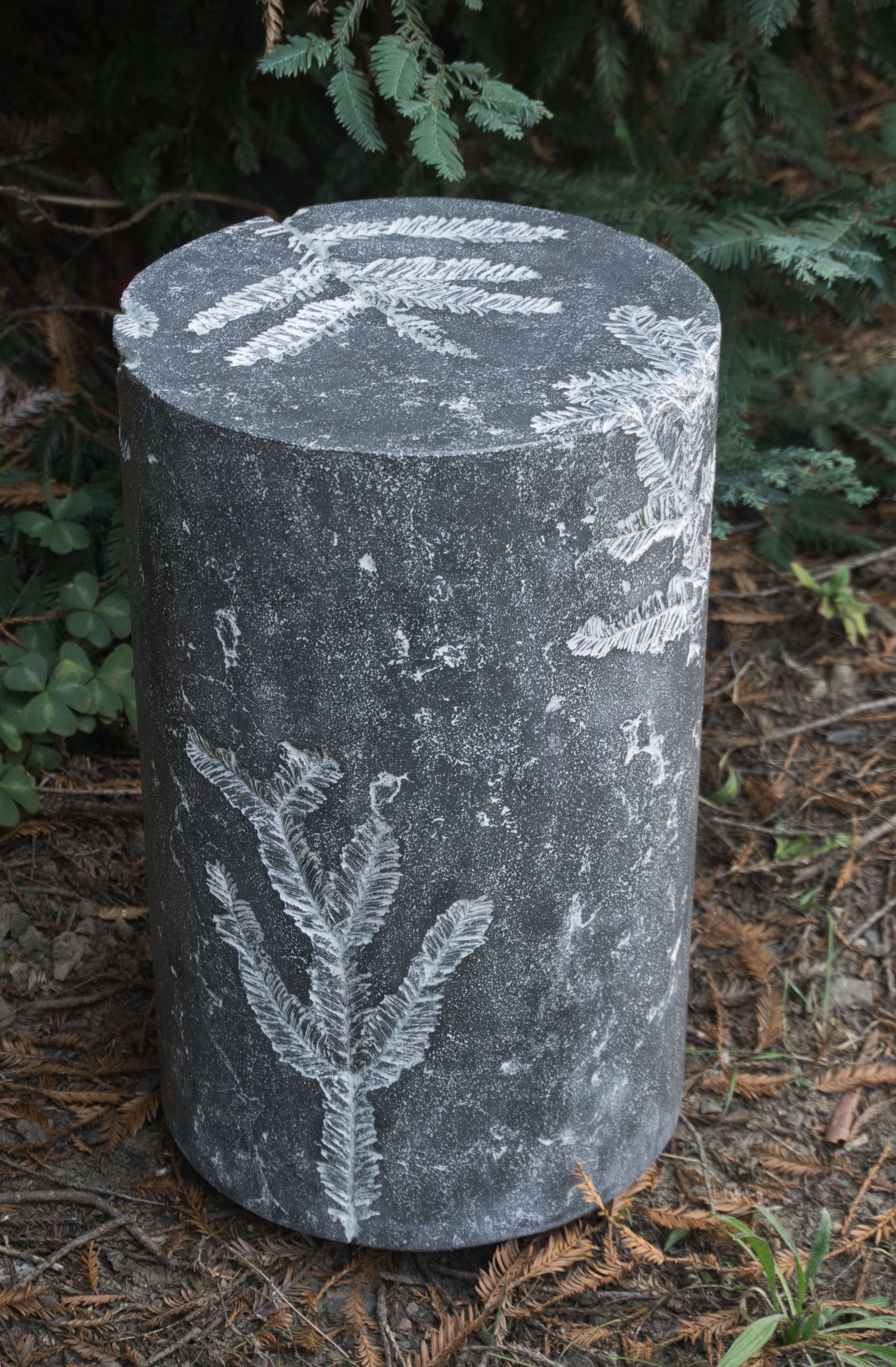 dark gray round concrete accent table with redwood leaves imprinted in top and sides and filled with white grout