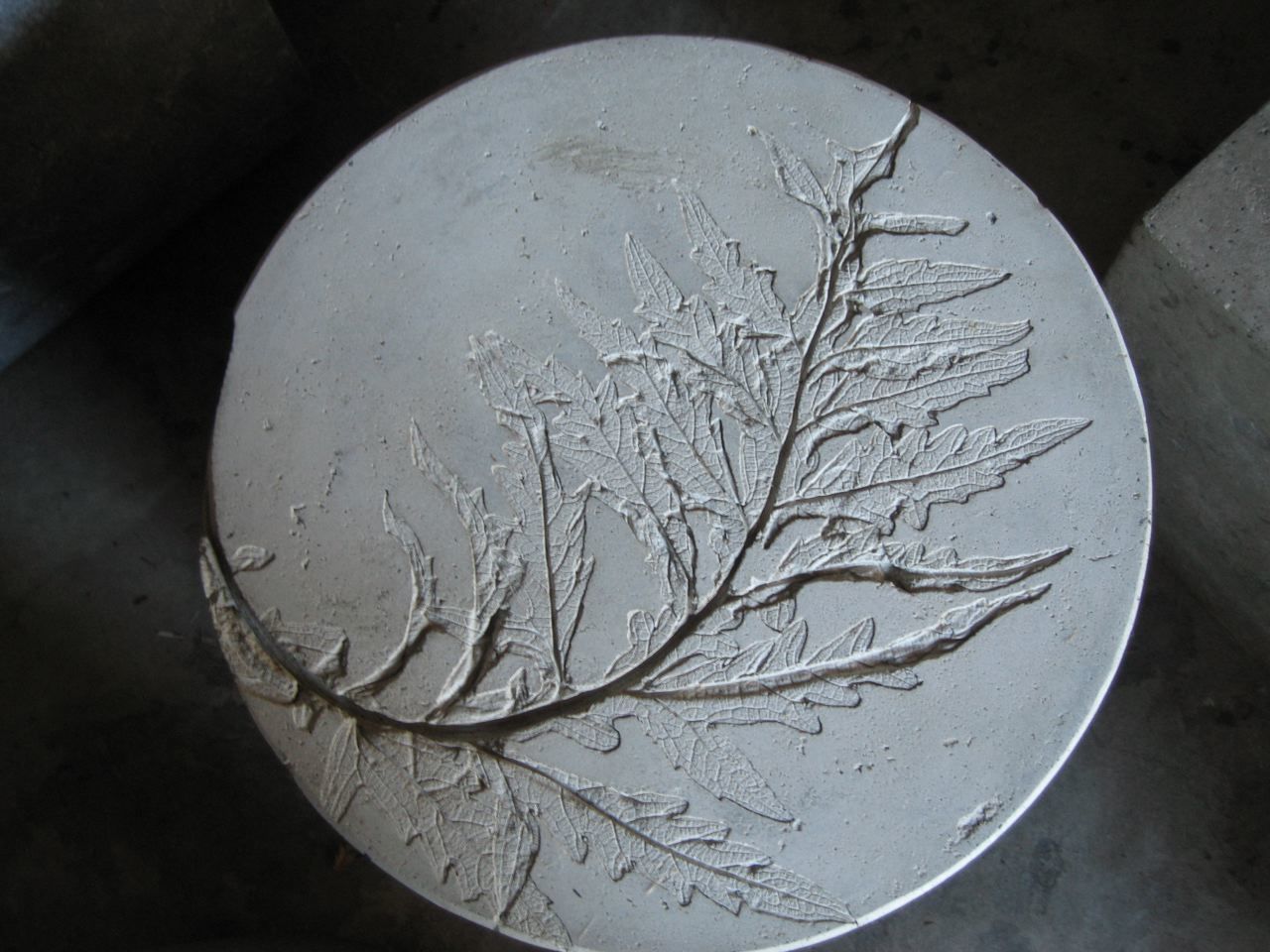 rustic fossil-like imprint of a curved artichoke leaf in round concrete accent table