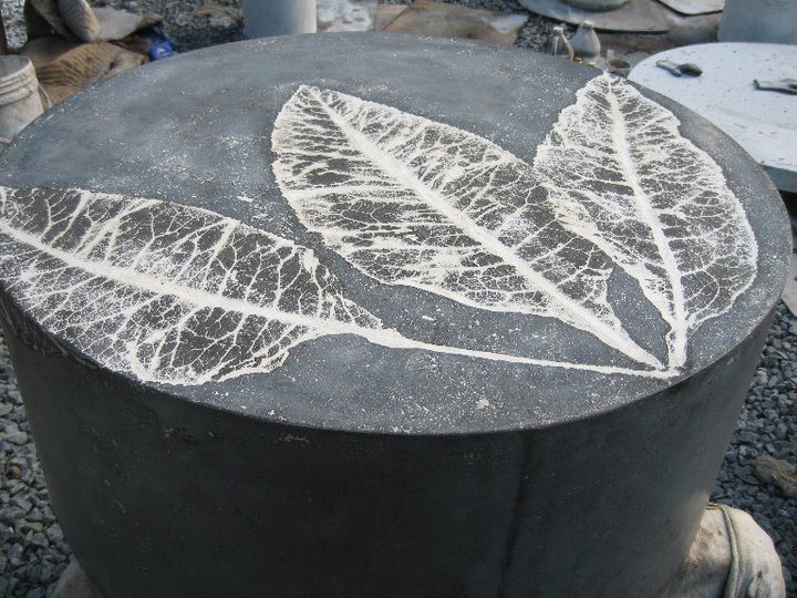 large cylindrical dark gray concrete coffee table with design of three white leaves on top