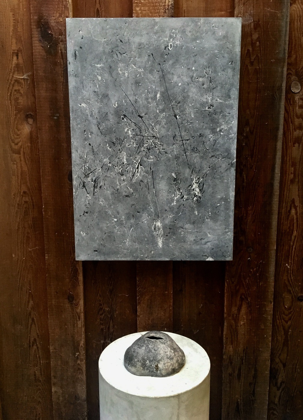 grey concrete wall panel with abstract grass impressions on wood wall with clay sculpture on plinth in front