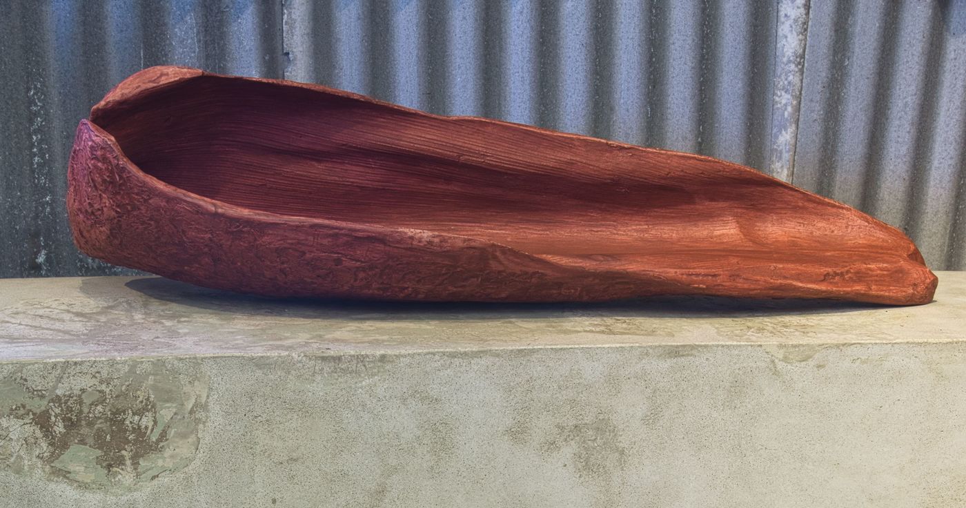 organic red concrete sculpture of palm seedpod sitting on concrete bench