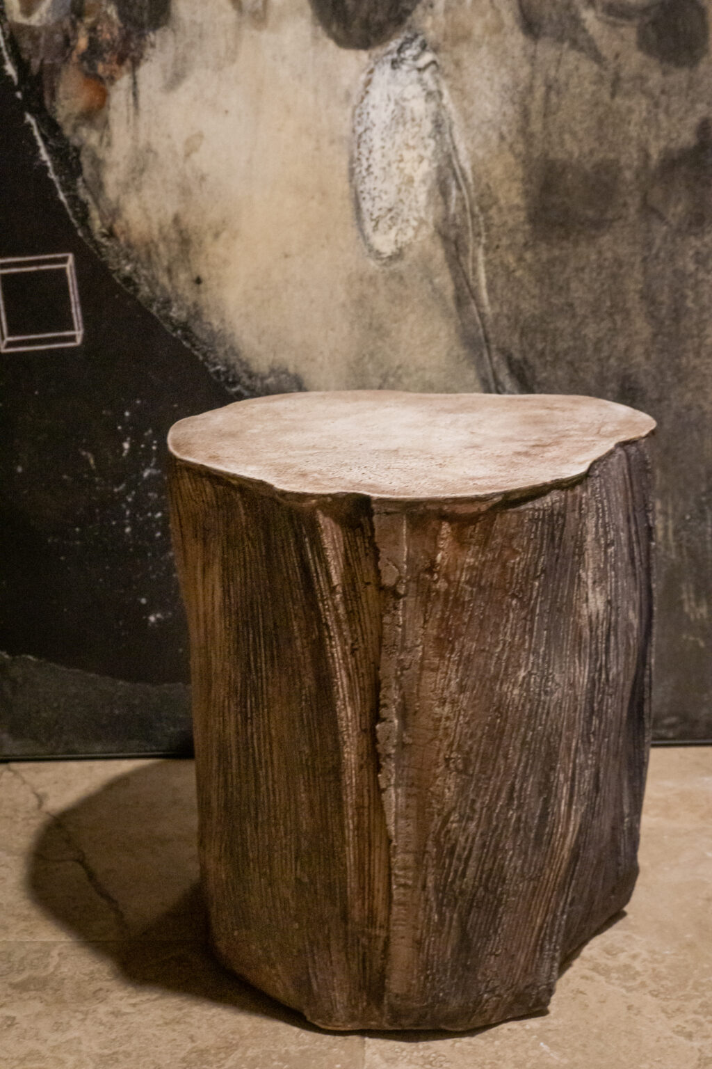 Small sculptural concrete table with palm seedpod texture in brown with abstract painting in background