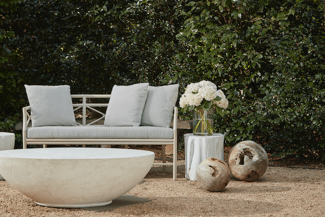 Outdoor living room scene with white oval concrete coffee table with palm seedpod concrete white table in background