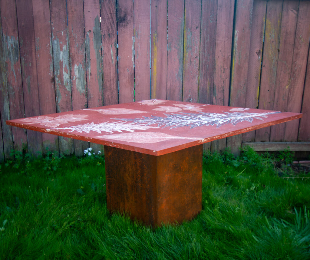 red concrete dining table top on orange square steel patina base sitting in grass